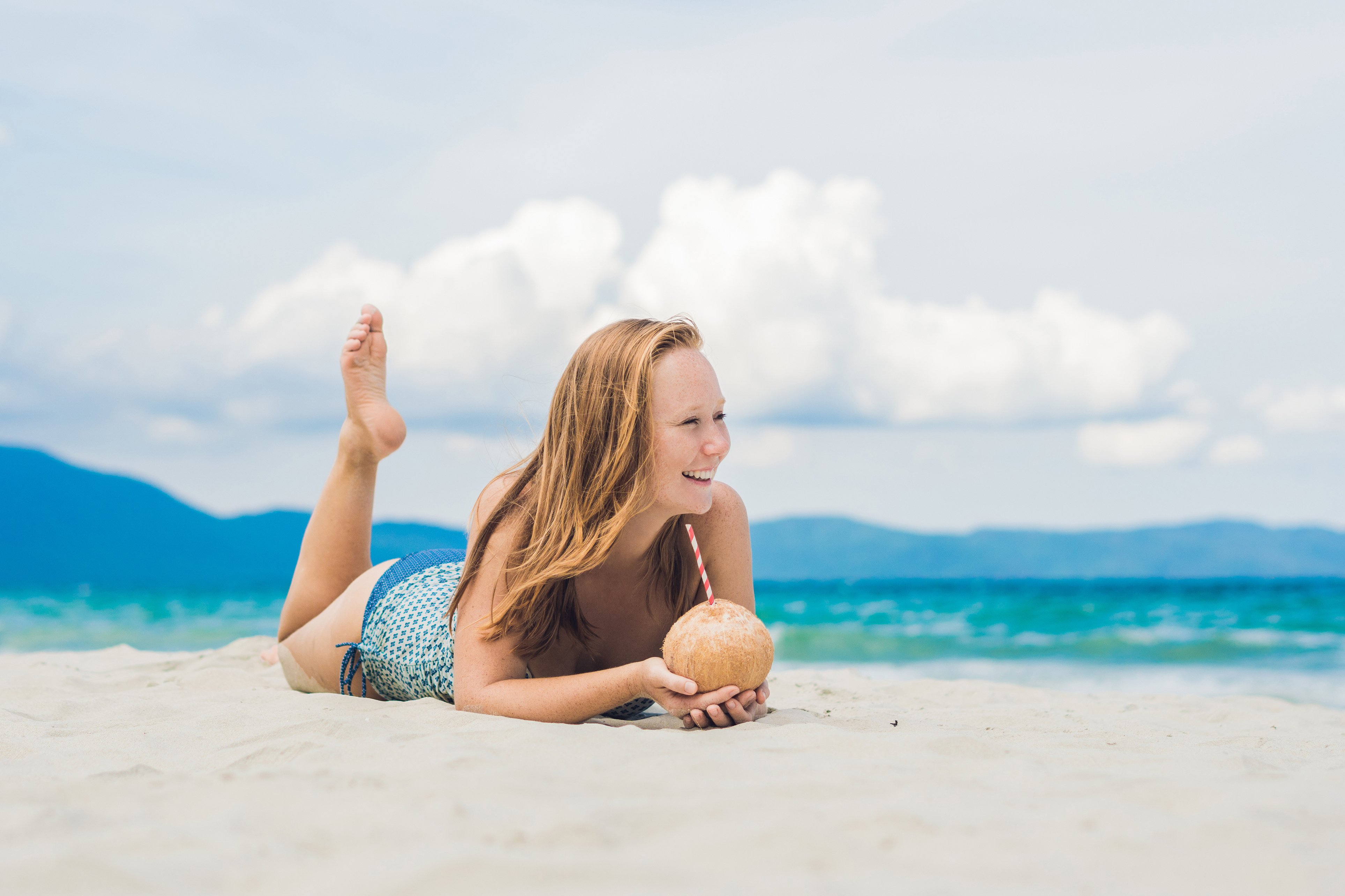 Young woman drinking coconut milk on beach.